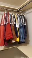 Closet view showing nine assorted women's jackets hanging on a rod, some covered with clear garment bags.