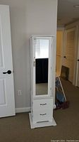 Front view of tall white wooden jewelry chest with mirror door