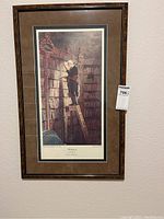 Full view of framed print showing an elderly man reading a book on a ladder surrounded by numerous bookshelves and books.