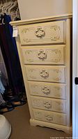 Front view of the cream lingerie chest showing six drawers with floral accent molding and decorative handles.
