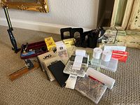 Wide angled photo showing the collection of office supplies including the vintage postal scale, calculators, notebooks, rubber bands, post-its, bookends, hole punch, a small light, and Nikon Realtree binoculars.