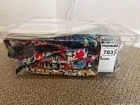 Six Vera Bradley brand purses stacked inside a clear plastic storage bin showing colorful floral patterns and quilted fabric.