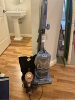 Photo showing upright Shark vacuum with attached handle and base, black carrying/storage bag beside it, and handheld vacuum in front with cords wrapped