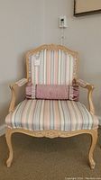 Front view showing detailed wood carving on the top rail and legs, striped upholstery, and pink bolster pillow with ruffles on the seat.