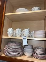 Cabinet with multiple stacks of plates and teacups featuring floral patterns in white and pink.