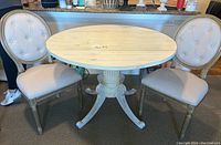 Front view of white round drop leaf table with two upholstered chairs on sides