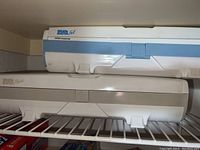 Two Wrap Master plastic wrap dispensers stacked on a shelf; one white with blue accents and one white with tan accents.