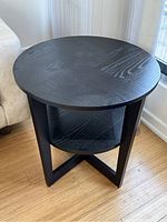 Round dark wood grain side table shot at an angle showing the top and one side with lower shelf and legs.