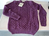 Full flat lay of dark purple cable knit sweater showing front design, ribbed hem and cuffs.