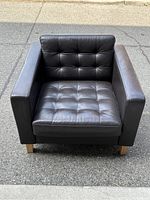 Front view of dark brown vinyl armchair showing tufted cushion details and wooden legs.