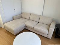 Side angle view of beige microsuede sectional sofa with chaise lounge, showing fabric texture and wooden legs.