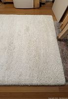 Overhead view of white shaggy rug on wooden floor and partly overlapping another patterned rug.