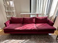 Front view of modern pink velvet 3-seater sofa with sunlight casting shadows. Shows general shape and three cushions.