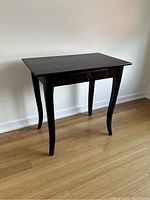 Side table with single drawer shown from an angled side view highlighting the curved legs.