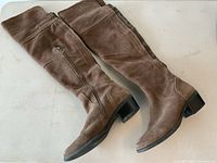 Side angle view showing the full length and outer side of both brown suede knee high boots with visible zipper and block heel.