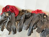 Lot of six women's motorcycle jackets displayed on a white padded surface, showing black and red jackets.
