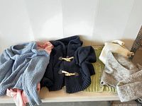 Overview of the 6 sweaters arranged on a surface showing varied colors and styles, including a navy blue toggle closure hoodie cardigan.