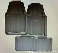 Four black rubber universal car floor mats arranged on a surface, two larger front mats with textured geometric tread, two smaller rear mats with grid pattern.