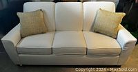 Frontal view of white sofa with two beige throw cushions in an unfinished setting