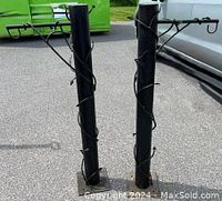 Two matching solid black iron posts with decorative vine-shaped iron accents spiral around the posts and include hooks at the top for hanging. Mounted on square base plates.