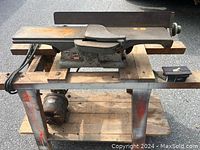 Photo showing vintage Craftsman jointer on metal stand with motor and power cord. Rust visible on tables and fence.