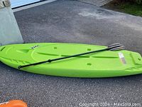 Side view of lime green plastic Pelican paddleboard showing length and shape with black paddle on top.
