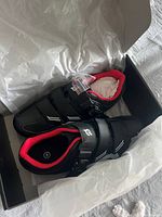Brand new black Peloton women's cycling shoes with red interior, displayed in open box with packing paper.