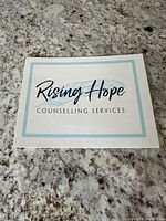 Photo of the Rising Hope Counselling Services gift certificate showing the company name and branding on a stone countertop.