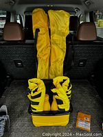 Two folded yellow beach chairs in carrying bags inside a yellow cooler placed on a car trunk floor