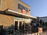 Exterior patio and entrance of The Duchess Pub with seating and black metal fencing, Canadian flag and sign visible.