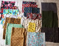 Photo shows 15 assorted pieces of printed cotton fabric in various colors and patterns, displayed flat.