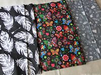 Three pieces of printed cotton fabric side by side showing patterns: white feathers on black, colorful butterflies on black, bunnies on grey.