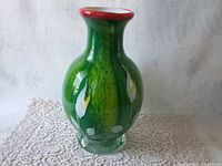 Front view of green art glass vase with white calla lilies on a lace background.