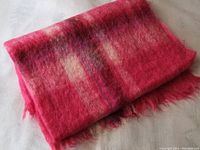 Folded red and pink plaid mohair wool blanket with fringed edges.