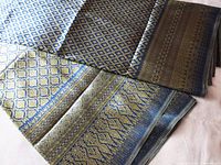 Two pieces of folded brocade fabric showing intricate patterns in blue and gold with shimmering gold thread