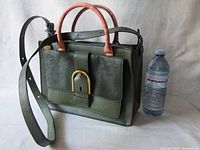 Fossil handbag in green leather with pink handles and gold buckle, placed next to a water bottle for size reference.