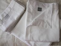 Folded white hemstitch tablecloth and a stack of napkins showing fabric texture and hemstitch detail.