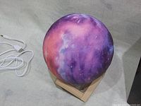 Moon lamp showing vibrant galaxy colors on wooden stand with USB cable nearby.