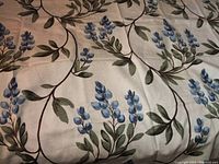 Close-up image showing the blue floral and leafy botanical print on natural beige cotton fabric.