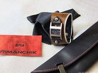 Photo showing the Rimanchik watch with its unique wide brown cuff leather band and the black leather pouch and red cleaning cloth laid beside it.