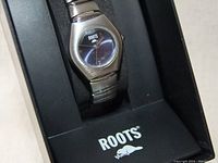 Close-up photo of the silver-tone Roots ladies wristwatch set inside the black Roots branded box.