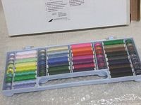 Plastic case containing 32 thread spools and 32 bobbins in multiple colors, laid out flat from above.