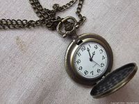 Front of the pocket watch pendant showing the white dial with black numerals and hands, opened lid showing quartz movement dial
