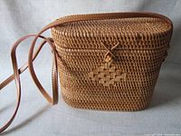 Front and side view of the new woven shoulder bag with leather strap and clasp closure, placed on beige fabric background.