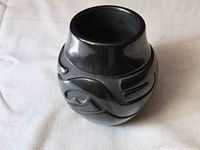 Angled front view of blackware vase showing carved Avanyu design and high polish finish