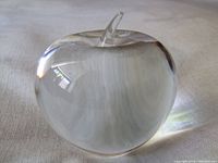 Clear, polished crystal apple with a small stem on top, showing rounded shape and transparency.