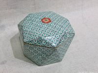 Closed view of the origami-shaped porcelain trinket box showing the detailed green and white diamond pattern with a central floral design on the lid and gold edging.