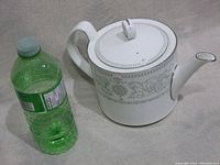 Full side view of the teapot with water bottle for size comparison showing its large size and overall design.
