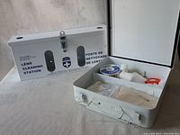 Photo of closed and open white metal boxes with first aid and lens cleaning supplies visible inside one box.