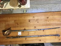 Full length sword and scabbard laid on wooden surface, showing blade length and overall sword condition.